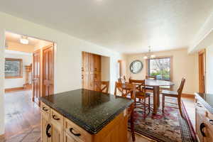 Kitchen featuring light wood-style floors, a center island, a chandelier, hanging light fixtures, and dark stone counters