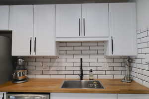 Kitchen with wood counters, decorative backsplash, and white cabinets
