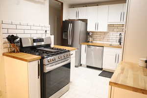Kitchen featuring butcher block countertops, appliances with stainless steel finishes, a sink, and tasteful backsplash