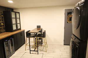 Dining area featuring wine cooler, stacked washing machine and dryer, recessed lighting, a dry bar, and baseboards