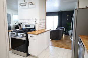 Kitchen featuring wooden counters, appliances with stainless steel finishes, white cabinetry, tasteful backsplash, and light wood finished floors