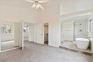 Carpeted bedroom featuring a spacious closet, ensuite bath, high vaulted ceiling, baseboards, and a ceiling fan
