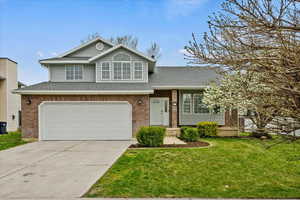 Tri-level home with a front lawn, an attached garage, brick siding, a shingled roof, and concrete driveway