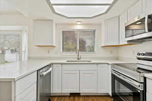 Kitchen with appliances with stainless steel finishes, a sink, white cabinetry, a peninsula, and light countertops