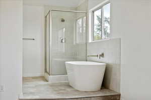 Bathroom featuring a stall shower, a soaking tub, and tile walls