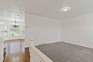 Empty room featuring a chandelier, a wainscoted wall, wood finished floors, and baseboards