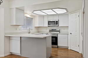 Kitchen featuring stainless steel appliances, a peninsula, wood finished floors, and white cabinetry