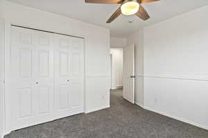 Unfurnished bedroom featuring dark colored carpet, baseboards, a closet, and a ceiling fan