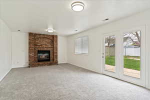 Unfurnished living room with healthy amount of natural light, carpet floors, a brick fireplace, and baseboards