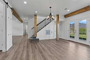 Unfurnished living room featuring beamed ceiling, recessed lighting, a chandelier, a barn door, and wood finished floors