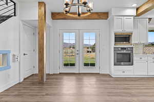 Kitchen with a chandelier, french doors, stainless steel appliances, white cabinetry, and beamed ceiling
