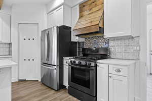 Kitchen featuring gas range, white cabinets, tasteful backsplash, light countertops, and custom exhaust hood
