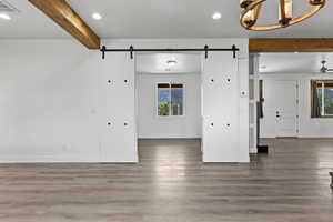 Unfurnished living room featuring a barn door, beam ceiling, plenty of natural light, wood finished floors, and recessed lighting