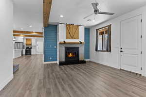Unfurnished living room featuring a barn door, recessed lighting, a ceiling fan, wood finished floors, and a glass covered fireplace