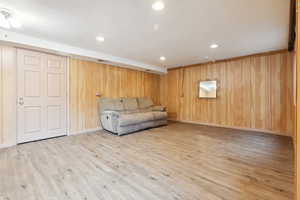 Unfurnished living room with wood finished floors, wooden walls, recessed lighting, and baseboards