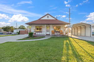 View of front of house featuring a detached carport, covered porch, a front yard, a shingled roof, and concrete driveway