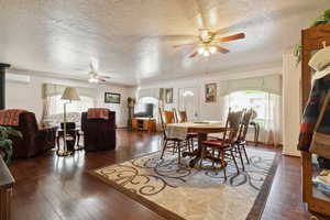 Dining area featuring a ceiling fan, a textured ceiling, ornamental molding, wood-type flooring, and a wall unit AC