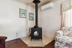 Detailed view of an AC wall unit, a wood stove, wood finished floors, and crown molding