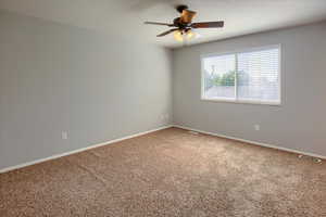 Carpeted spare room featuring ceiling fan and baseboards