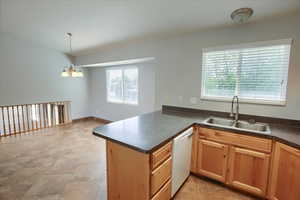 Kitchen featuring white dishwasher, a sink, a chandelier, dark countertops, and a peninsula
