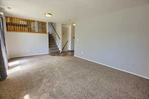 Empty room featuring stairs, carpet flooring, and baseboards
