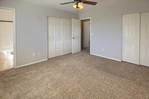 Unfurnished bedroom with baseboards, two closets, carpet floors, and ceiling fan