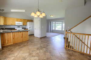 Kitchen featuring white appliances, a sink, a chandelier, vaulted ceiling, and decorative light fixtures