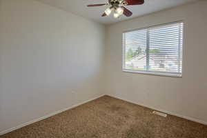 Carpeted spare room with a ceiling fan and baseboards
