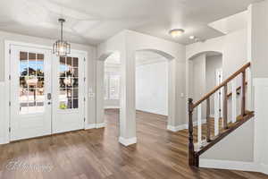 Foyer entrance with dark wood-type flooring, a textured ceiling, baseboards, arched walkways, and stairway