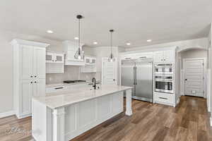 Kitchen with appliances with stainless steel finishes, a sink, dark wood-style flooring, white cabinets, and a kitchen island with sink