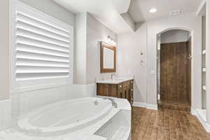Bathroom with vanity, a jetted tub, wood finished floors, baseboards, and recessed lighting