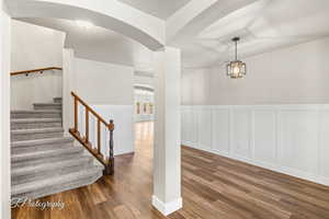 Stairway featuring arched walkways, a decorative wall, wood finished floors, and a wainscoted wall