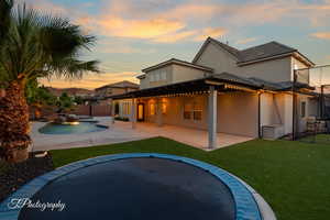 Back of property at dusk with stucco siding, a patio area, and a hot tub