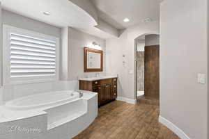 Bathroom with a bath, vanity, a tile shower, baseboards, and wood finished floors