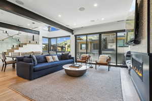 Living room with stairs, wood finished floors, a warm lit fireplace, and recessed lighting