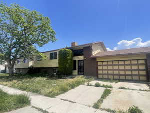 View of front facade featuring brick siding, a garage, a chimney, and concrete driveway