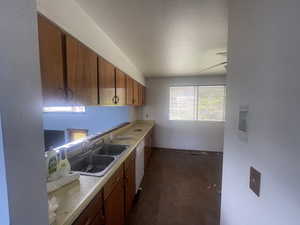 Kitchen featuring a sink, brown cabinetry, light countertops, white dishwasher, and a textured ceiling