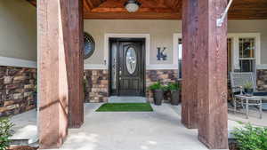 Doorway to property featuring stucco siding, stone siding, and a porch