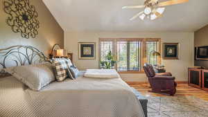 Bedroom with lofted ceiling, wood finished floors, baseboards, and ceiling fan