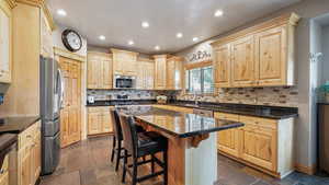 Kitchen with stainless steel appliances, light brown cabinetry, recessed lighting, and a kitchen bar