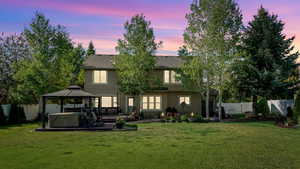 Back of property at dusk with a hot tub, a gazebo, stucco siding, a patio area, and a shingled roof