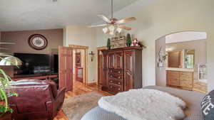 Bedroom with light wood-style floors, high vaulted ceiling, arched walkways, ensuite bath, and a ceiling fan