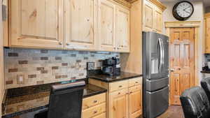 Kitchen featuring stainless steel fridge with ice dispenser, light brown cabinets, backsplash, and dark stone counters