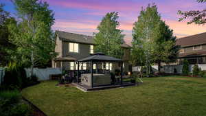 Back of house at dusk featuring a gazebo, a hot tub, and stucco siding