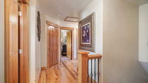 Hallway with light wood-style floors, baseboards, and an upstairs landing