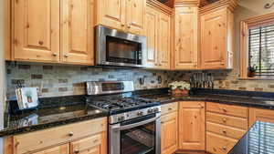 Kitchen featuring appliances with stainless steel finishes, backsplash, light brown cabinetry, and dark stone counters