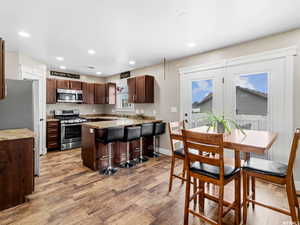 Kitchen with appliances with stainless steel finishes, light wood finished floors, recessed lighting, light countertops, and a breakfast bar