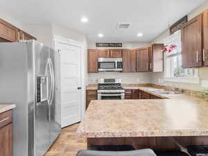 Kitchen with stainless steel appliances, a sink, light wood-type flooring, a kitchen bar, and a peninsula
