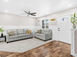 Living room featuring wood finished floors, ceiling fan, wainscoting, a decorative wall, and recessed lighting