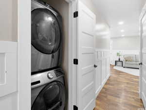 Laundry room with stacked washing machine and dryer, light wood-style flooring, wainscoting, and recessed lighting